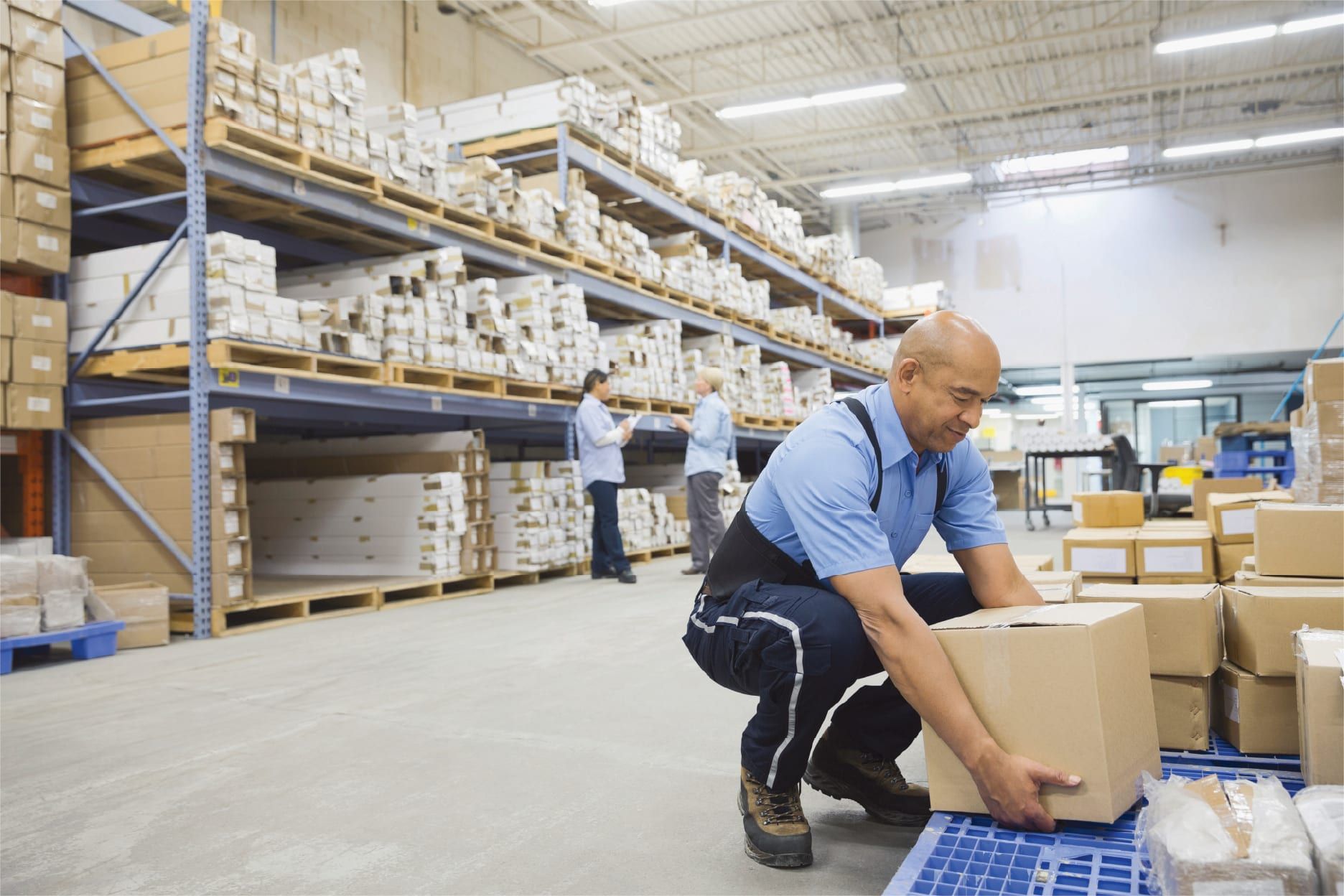 Man working in a warehouse squatting to pick up a box