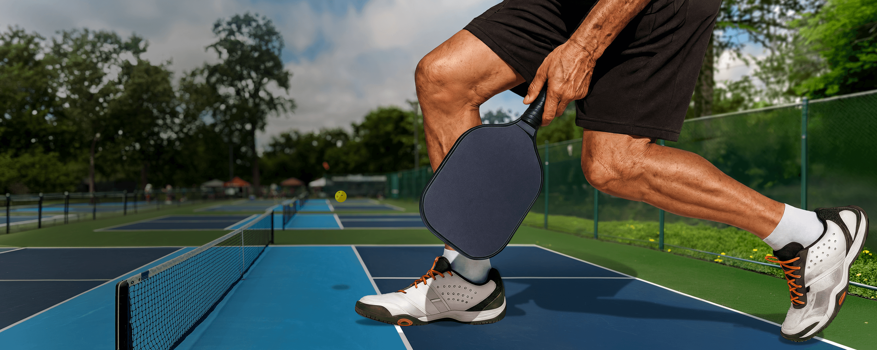 A disproportionately large pair of men's legs, visible from mid-thigh down, on a pickleball court.