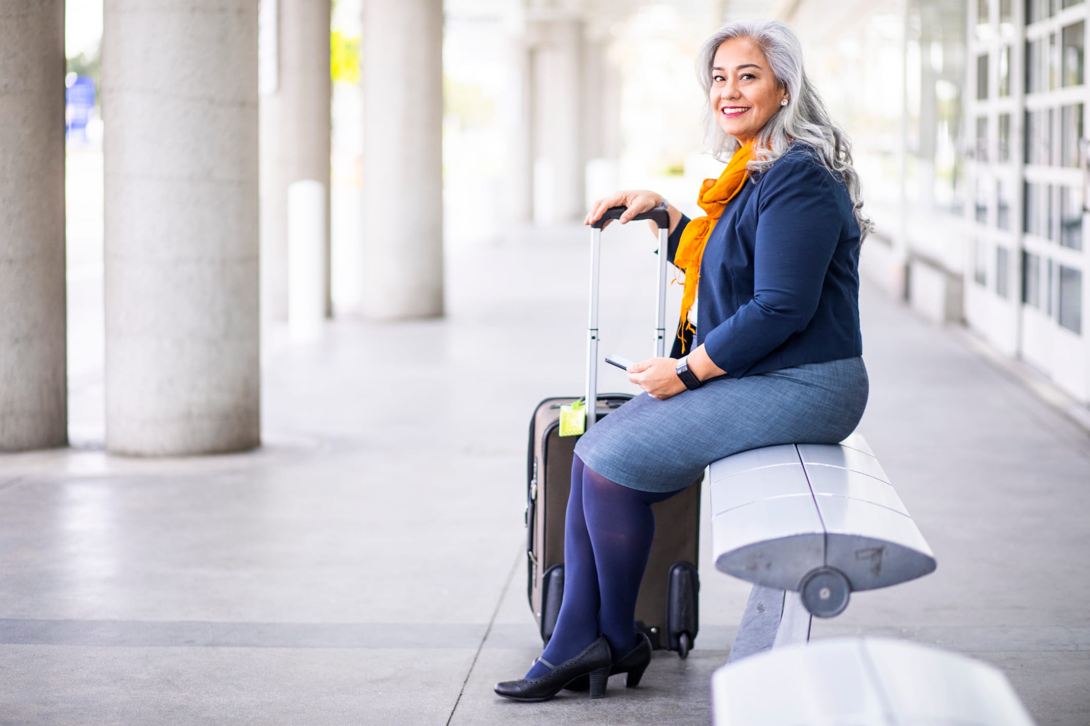 Woman with grey hair sitting outside an airport.